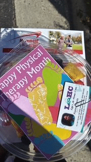 Clear glass bowl filled with colorful pamphlets promoting Physical Therapy Month, including one that reads 'Happy Physical Therapy Month'.